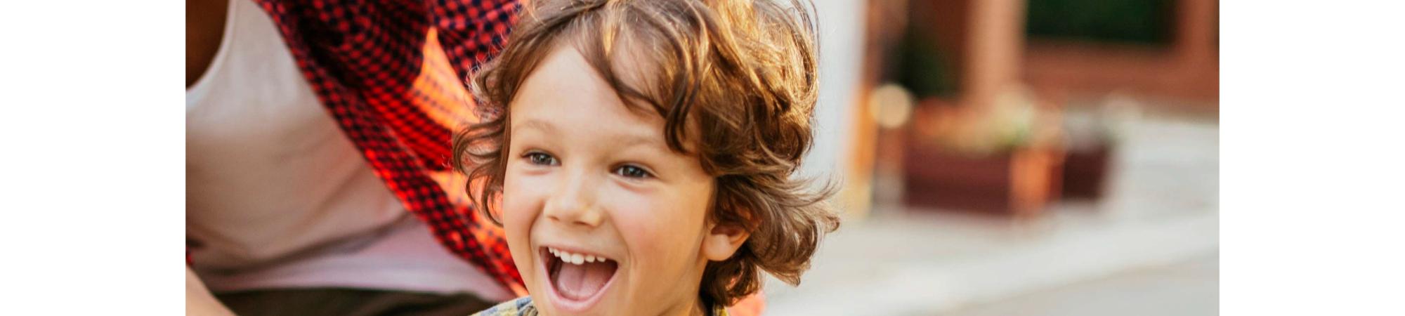 Boy riding bike and smiling while his father is supporting him.
